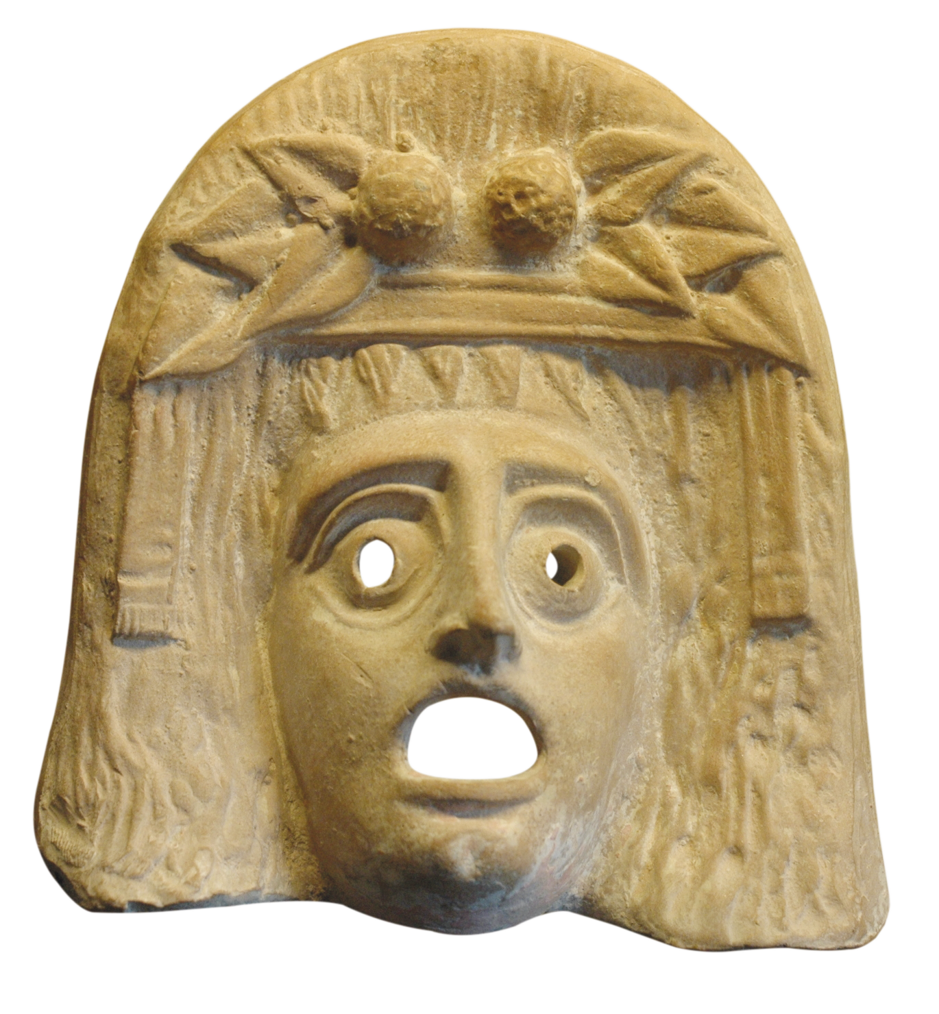 Fotografia. Máscara de pedra de figura mitológica. No alto, adornando a testa, há uma coroa de folhas e frutos. Há buracos para os olhos, que são representados arregalados, e para a boca, representada bem aberta.