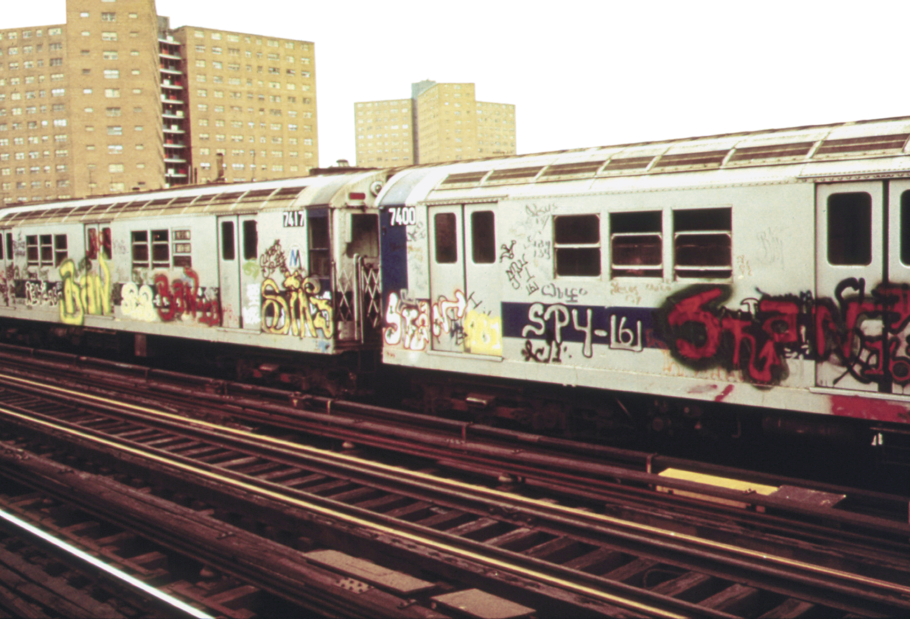 Fotografia. Vista de dois vagões de um metrô com grafite na parte externa.