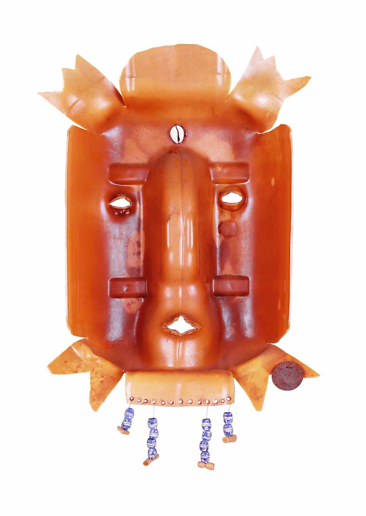Escultura. Máscara  criada por partes de garrafa plástica, aberta, em tons de marrom-claro. Há aberturas para os olhos e a boca. Na parte inferior, dependurados, há adornos feitos de contas e búzios.