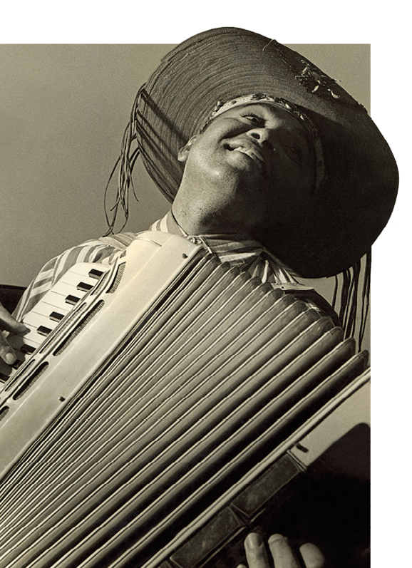 Fotografia em preto e branco. Retrato em perspectiva de baixo para cima, mostrando homem sorrindo enquanto toca uma sanfona. Ele usa chapéu nordestino de couro.