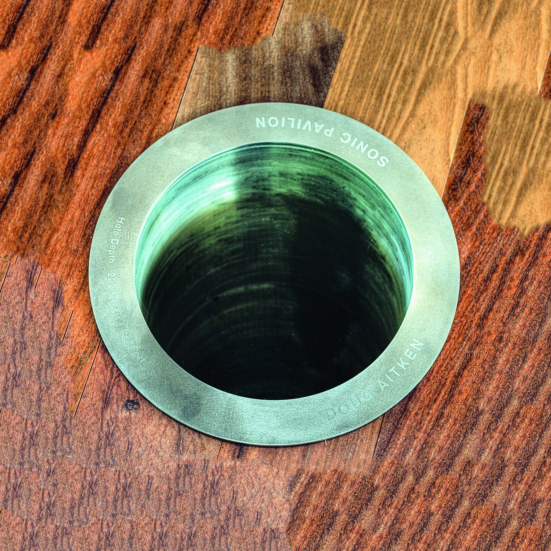 Fotografia. Destaque da abertura de um tubo circular metálico em uma superfície de madeira.