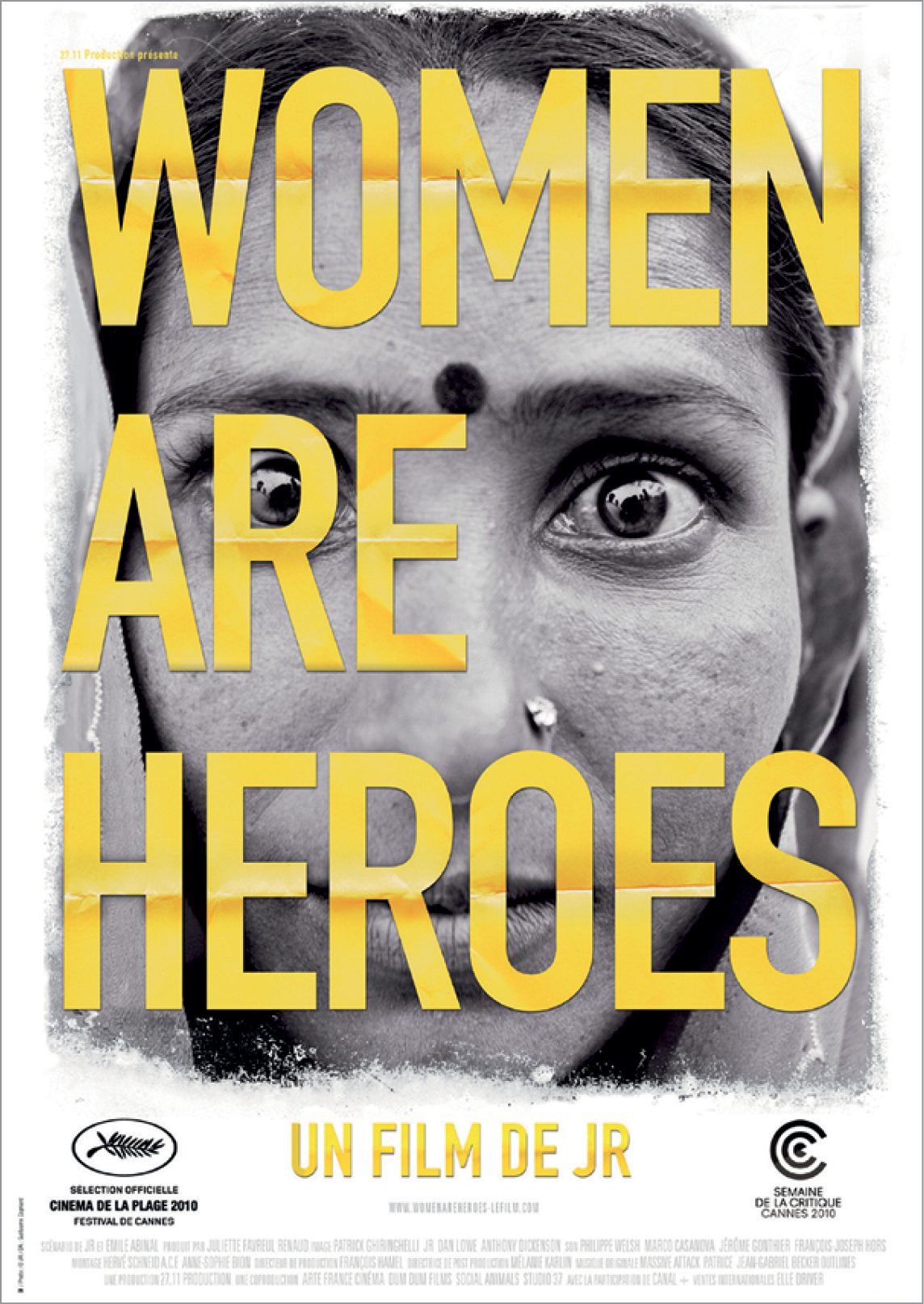 Fotografia. Capa de documentário. Fotografia em preto e branco de uma mulher com piercing no nariz e um ponto no centro da testa, usando lenço na cabeça. Sobre a imagem, há a frase Women are heroes.
