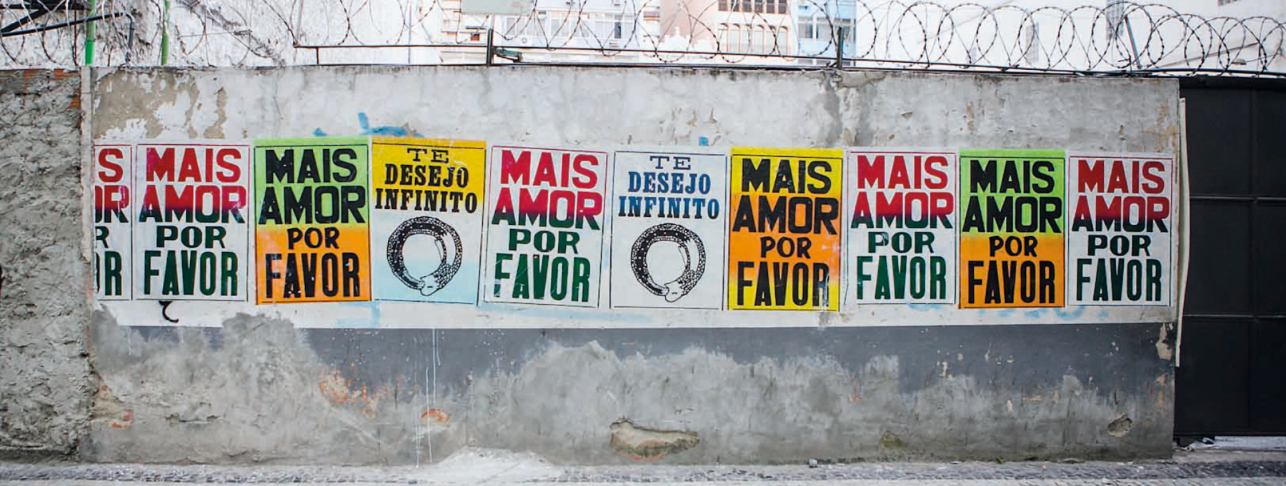 Fotografia. Muro com lambe-lambes coloridos e variados com as frases Mais amor por favor e Te desejo infinito.