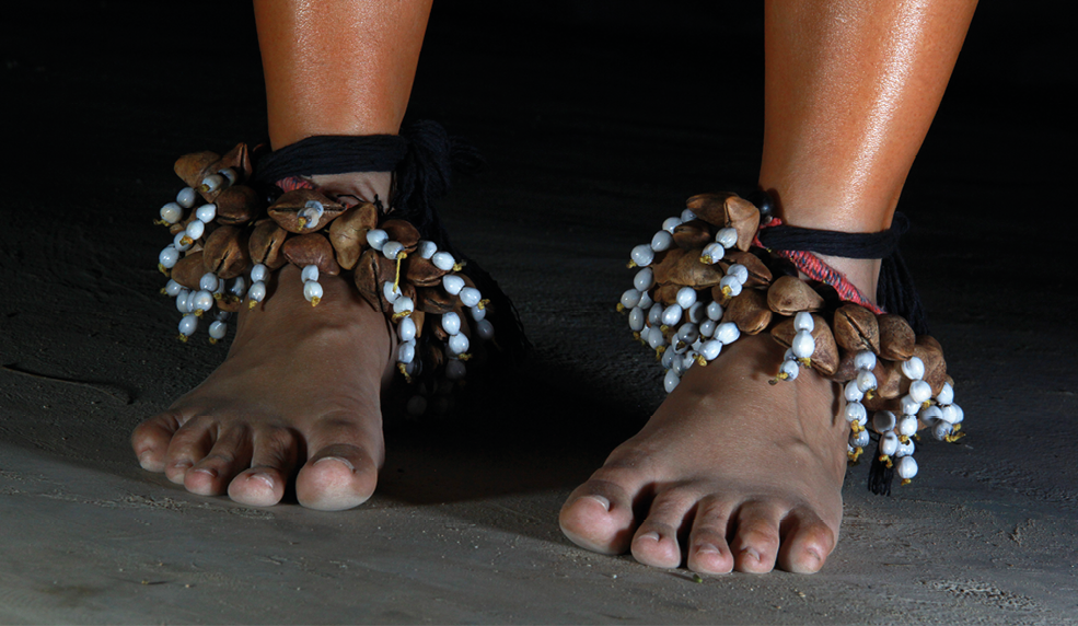 Fotografia. Destaque para tornozeleiras feitas com sementes marrons e brancas.