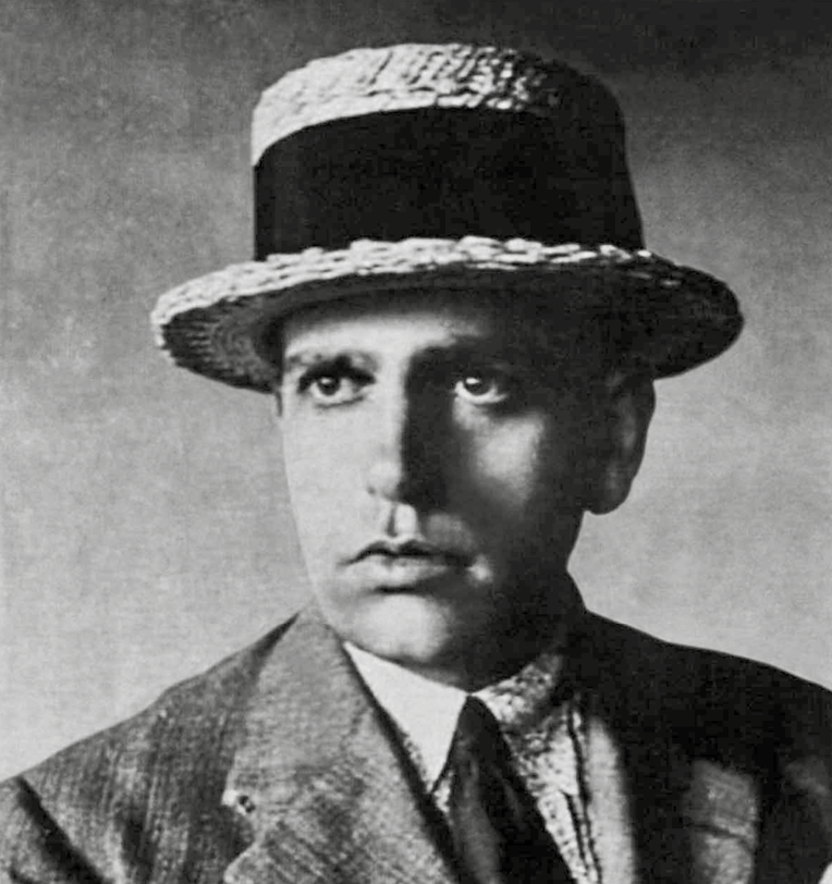 Fotografia em preto e branco. Retrato de um homem que usa chapéu arredondado e está vestido com paletó, gravata e camisa social.