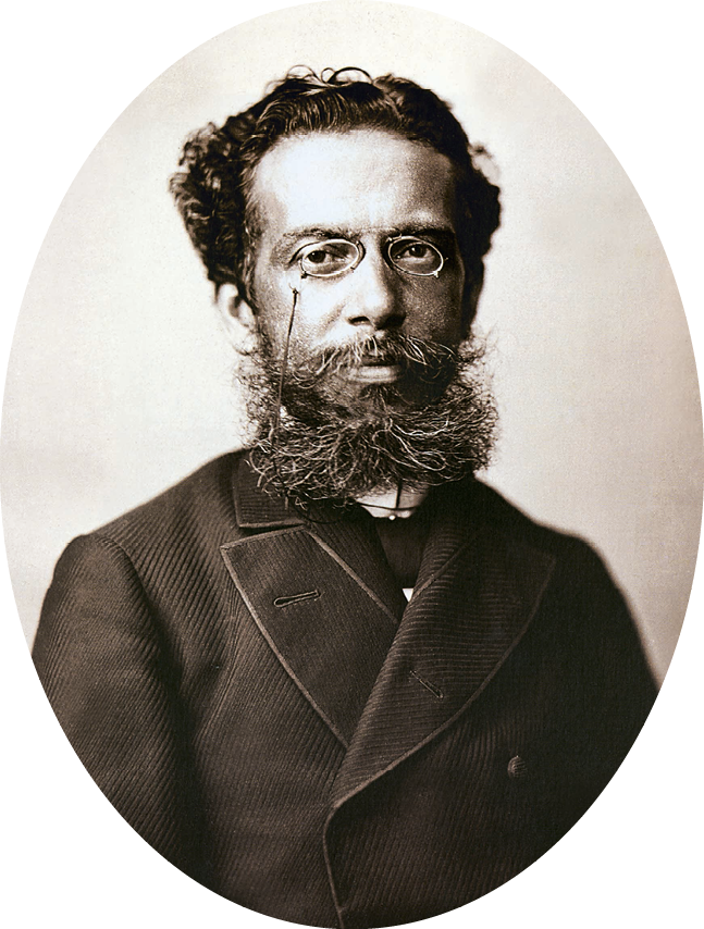 Fotografia em preto e branco. Homem de cabelo curto escuro e barba longa, com óculos de armação arredondada e paletó escuro.