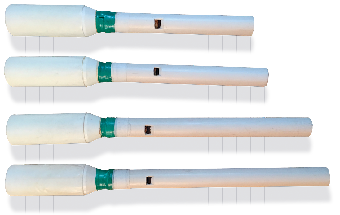 Fotografia. Quatro flautas feitas com tubos brancos de PVC. Na ponta de cada uma delas, embalagens plásticas, também na cor branca, foram coladas com fita verde.