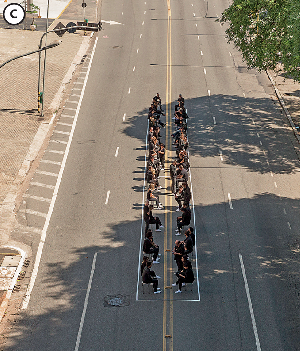 Fotografia C. Pessoas sentadas dentro de um retângulo do tamanho de um vagão de trem feito na rua.