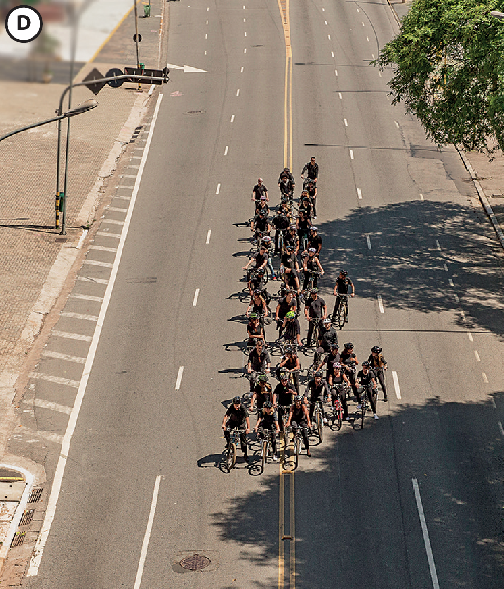 Fotografia D. Aglomerado de pessoas sentadas em bicicletas ocupando um pequeno espaço da rua.