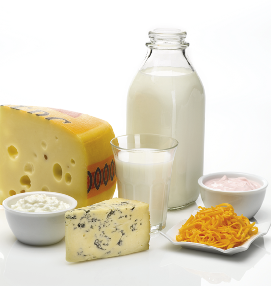 Fotografia. Um pedaço de queijo com buraquinhos; uma garrafa e um copo de vidro com leite; recipiente com um creme rosado; recipiente com alimentos amarelo e cortado em tiras; queijo com partes azuladas; recipiente com creme branco.