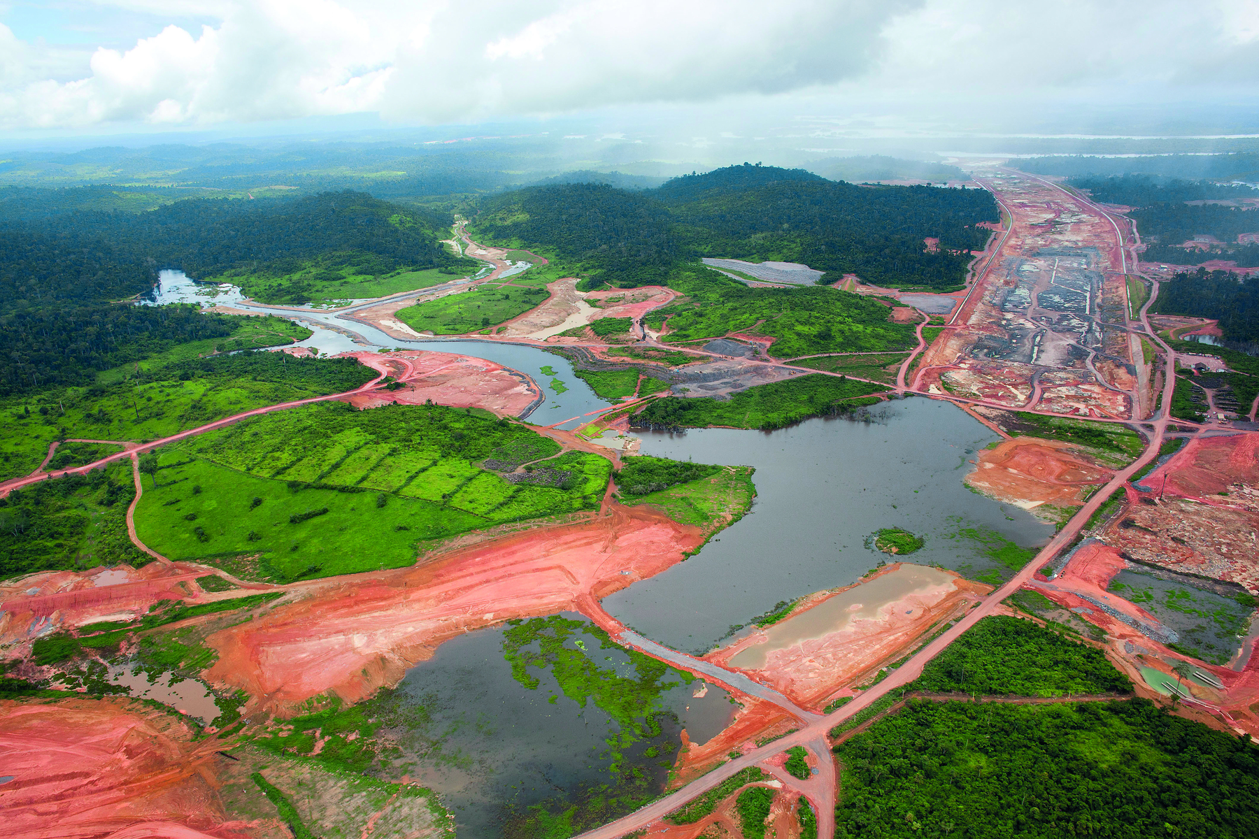 Fotografia. Vista aérea de uma grande área desmatada e alagada, com solo exposto e áreas conectadas por caminhos de terra. Há alguns pontos com vegetação preservada, sobretudo ao fundo, à esquerda, onde a formação vegetal está mais adensada.