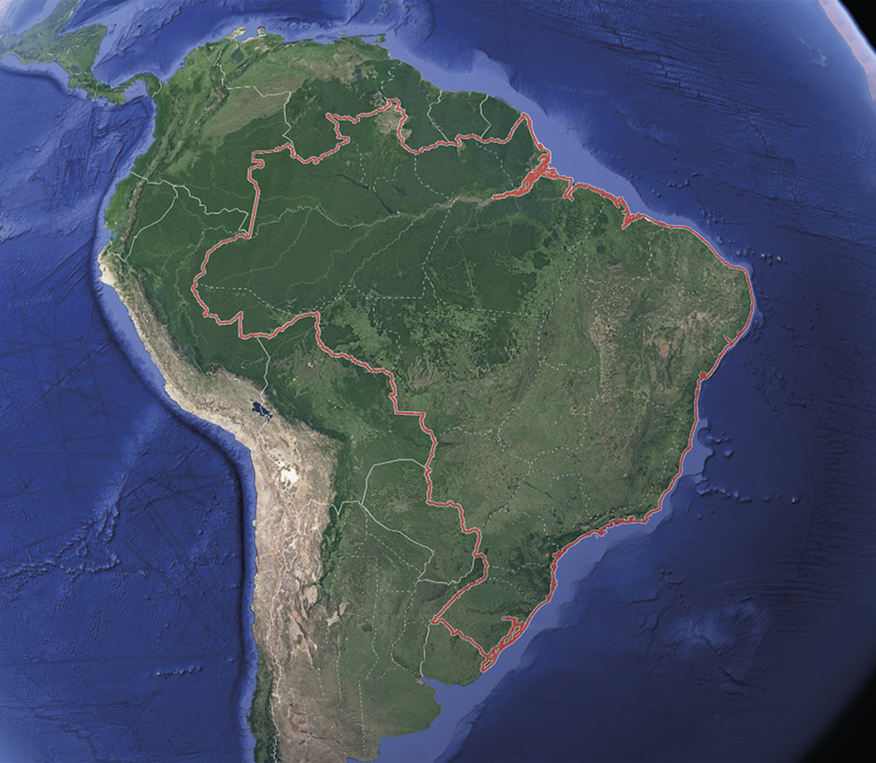 Imagem de satélite. A imagem enfoca a América do Sul e os oceanos que a margeiam, evidenciando as fronteiras dos países, a divisa entre as unidades da federação e o relevo oceânico. Na parte continental, há áreas em tons de verde, marrom e bege. As águas oceânicas são representadas em tons de azul. Uma linha vermelha contorna a fronteira terrestre do Brasil, destacando o país em relação às outras porções do território
