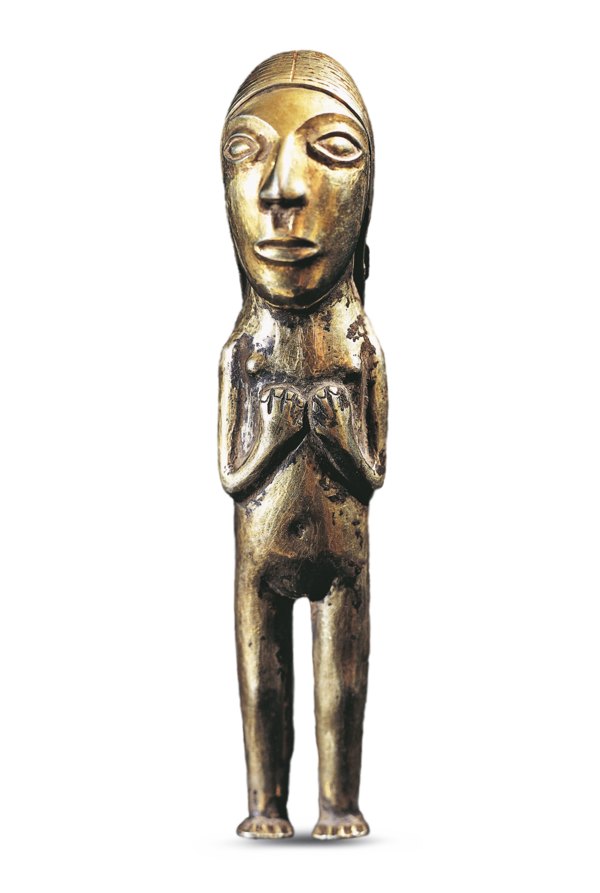 Fotografia. Estatueta de metal de cor dourada representando uma mulher. Ela tem a cabeça grande, o rosto comprido, olhos e nariz grandes, sobrancelhas e lábios grossos. Está nua, em pé, com as mãos sobre o peito e descalça.