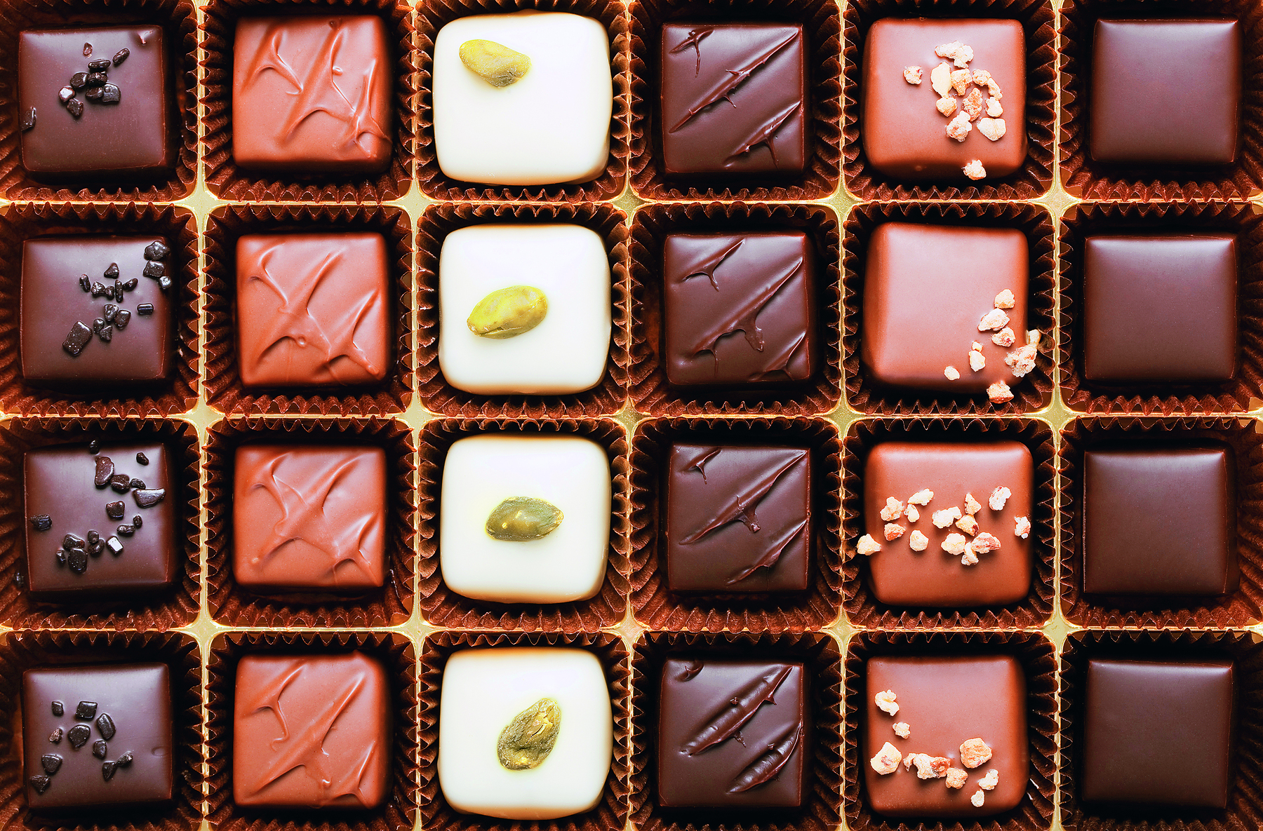 Fotografia. Caixa de bombons de chocolate de formato retangular, com 6 colunas e 4 fileiras.