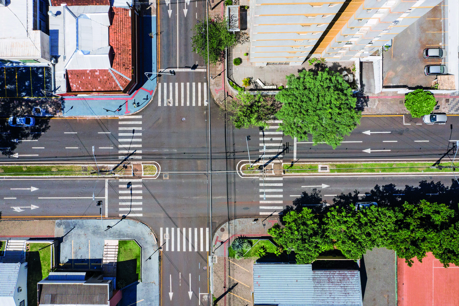 Fotografia. Vista área do cruzamento de de duas ruas. Em cada cruzamento tem faixas de pedestres. Na avenida Juscelino Kubitscheck tem um canteiro central gramado e com iluminação, separando as duas vias.