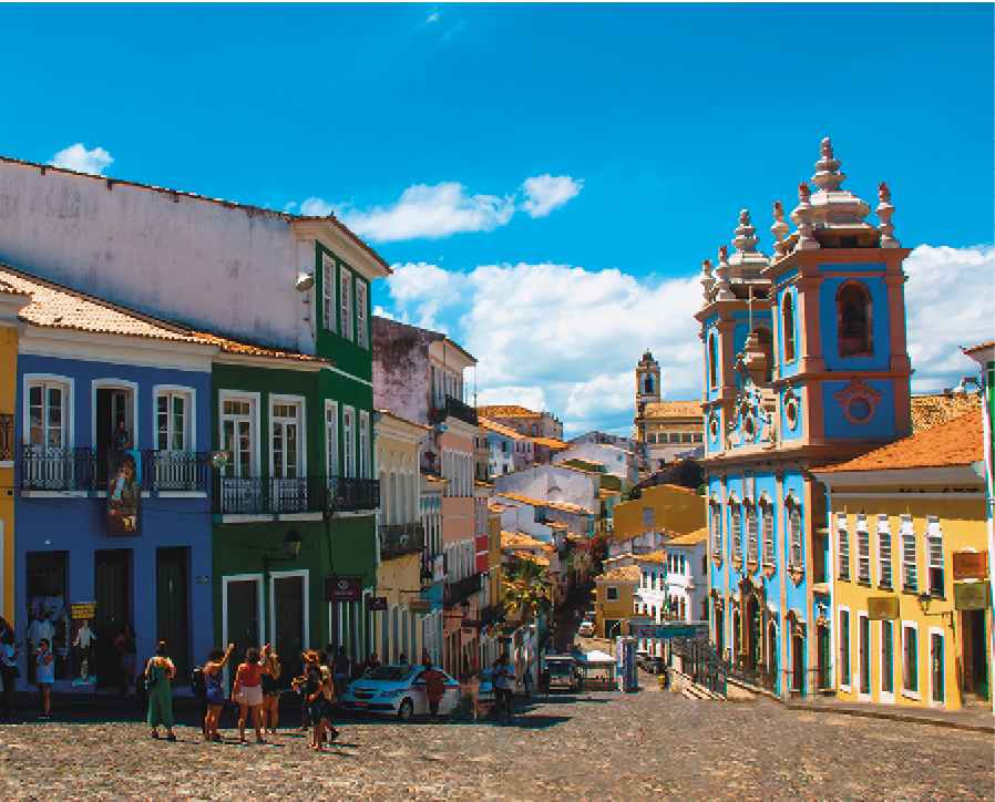 Fotografia. Local onde se localizava o pelourinho no
centro histórico da cidade de Salvador. Ao centro uma rua, à esquerda casas e à direita uma igreja. Ao fundo, céu azul com nuvens.