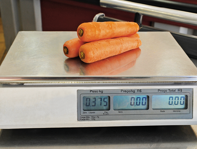 Fotografia. Três cenouras em cima de balança na cor branca e detalhes em cinza, com visor indicando 375 gramas.