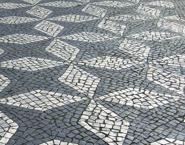 Foto. Calçada com padrão definido por composição de quatro losangos brancos unidos pelo vértice que contém a diagonal maior. O espaço livre entre os losangos forma figuras com oito lados.