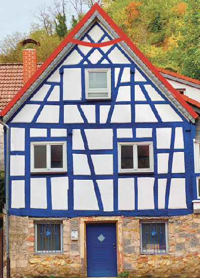 Fotografia. Vista frontal da casa que possui uma parte retangular branca com linhas tracejadas em azul e um telhado branco com linhas azuis. O telhado tem formato de triângulo. Em destaque vermelho, foi contornado ângulo agudo do vértice desse telhado. É possível identificar cinco janelas, sendo duas ao lado de uma porta, duas na parte retangular e uma centralizada na parte triangular.