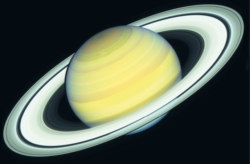 Fotografia. Fundo escuro com planeta amarelo e círculo ao redor representando os anéis.