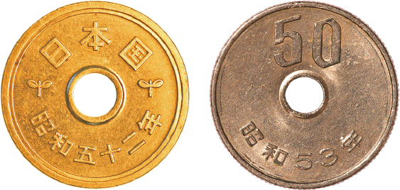 Fotografia. Moeda circular dourada vazada circularmente no centro com inscrições japonesas. Ao lado, moeda circular em tom de cobre com número 50, também vazada circularmente ao centro.