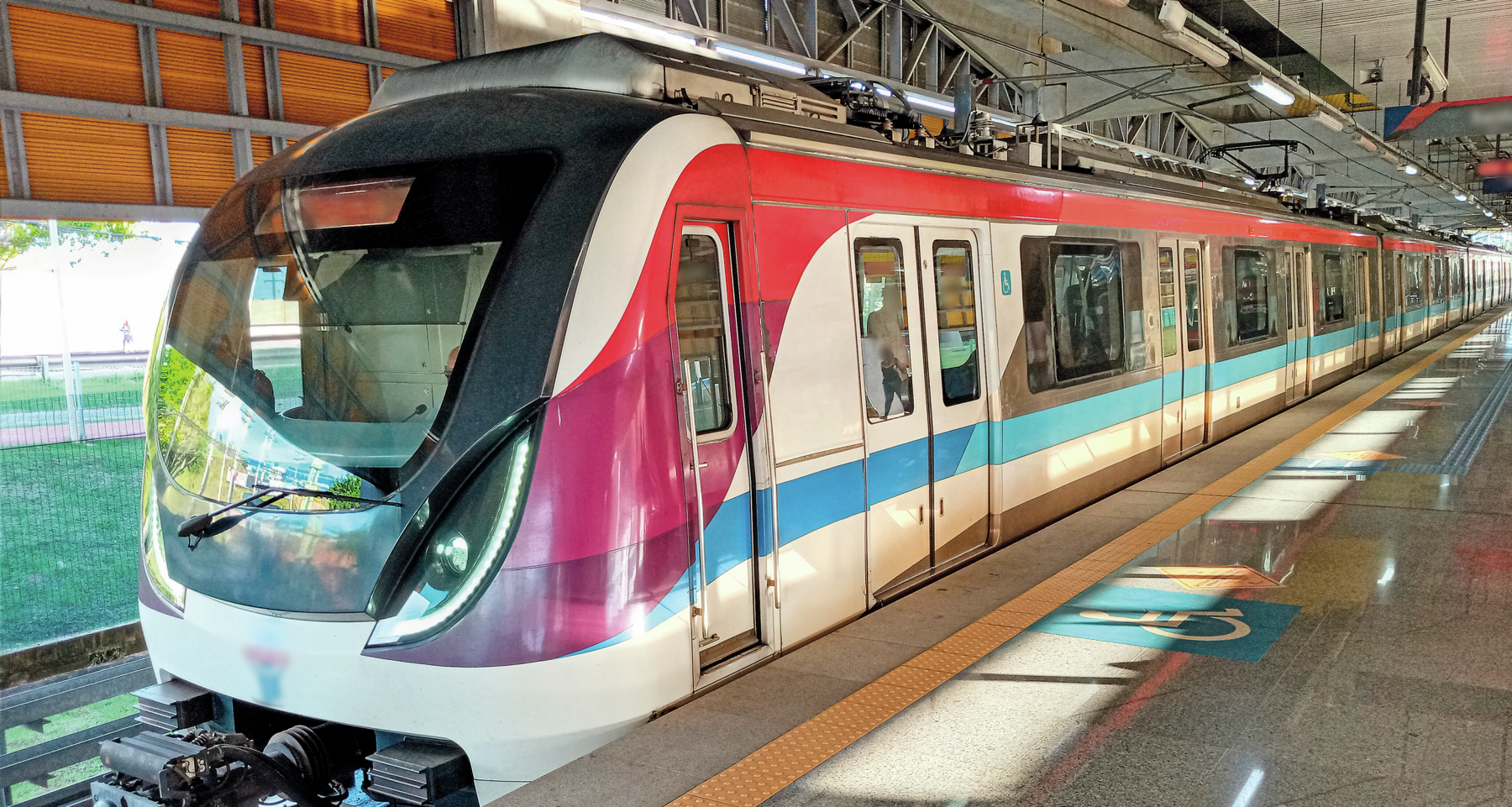 Fotografia. Em uma estação, metrô branco, vermelho e azul parado.