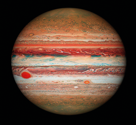Fotografia. Planeta Júpiter. Em fundo preto, esfera com a borda esfumaçada, com várias cores em faixas horizontais, com tons de vermelho, marrom, azul e alaranjado.