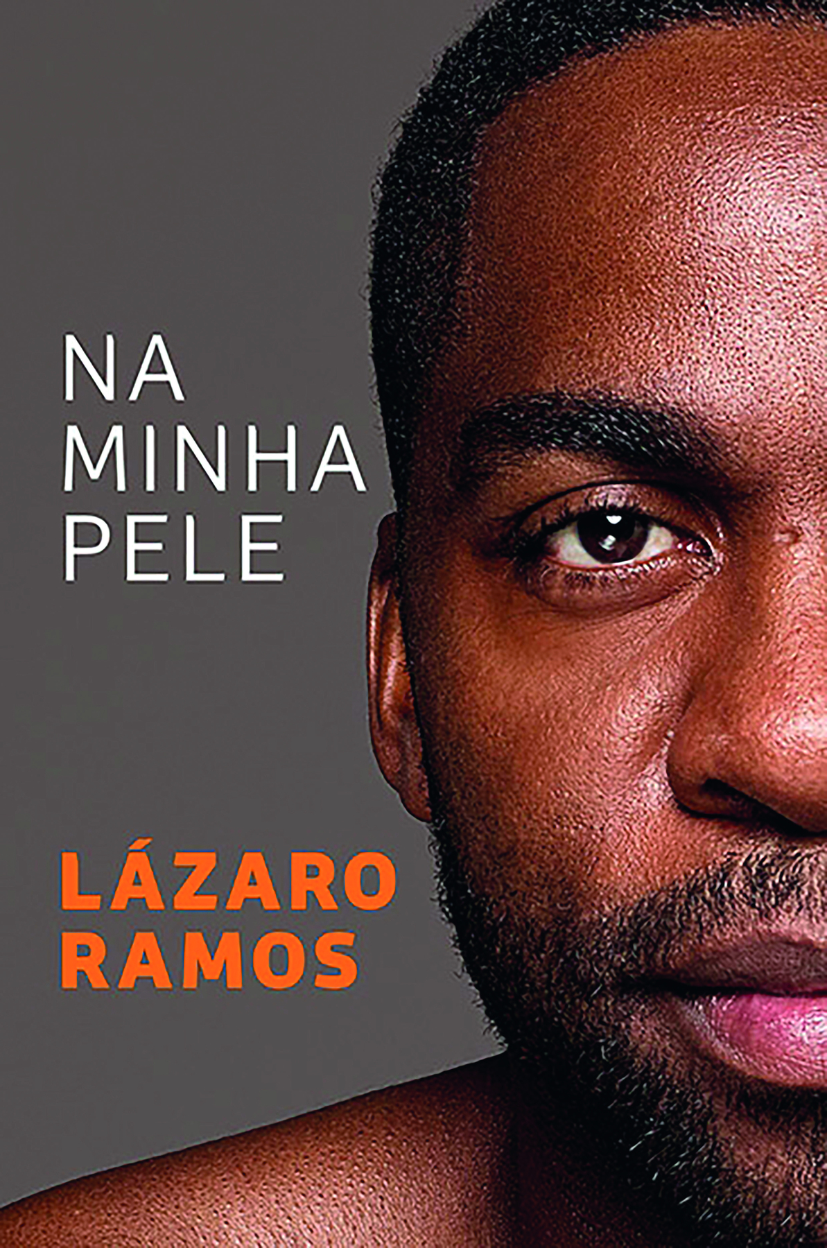 Capa de livro. Na parte superior à esquerda há o título do livro: NA MINHA PELE. Na parte inferior à esquerda há o nome do autor: LÁZARO RAMOS. À direita, há uma fotografia da metade direita do rosto de Lázaro, homem negro com barba e cabelos curtos.