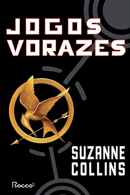 Fotografia. Reprodução de capa de livro. Na parte superior, o título: 'JOGOS VORAZES'. Abaixo, no canto direito, o nome da autora: 'SUZANNE COLLINS'. No centro da capa, sobre um fundo preto com traçados circulares e linhas retas cinza, ilustração de um anel circular dourado, no interior do qual há um pássaro semelhante a um beija-flor e uma seta, também dourados.