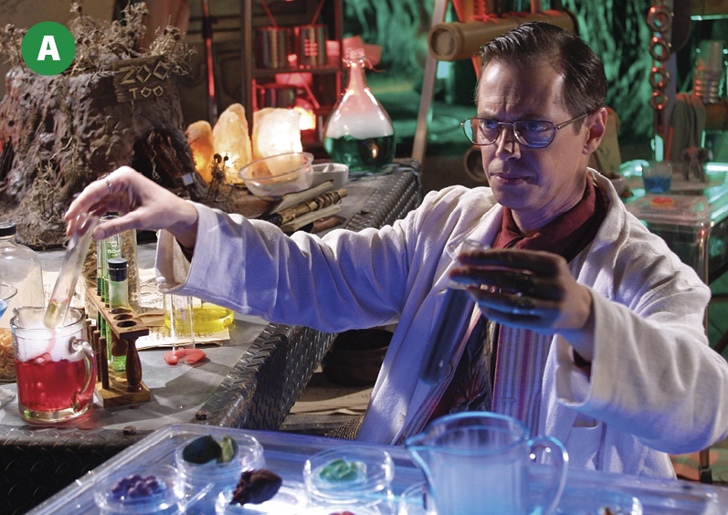 Fotograma. Um homem de óculos e avental branco com expressão séria manipula equipamento de laboratório, conduzindo um experimento científico. Ao fundo, diversos outros equipamentos de laboratório. A iluminação da cena é parcial.