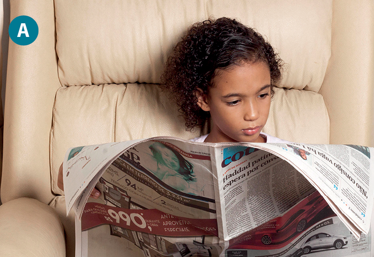 Fotografia A. Uma adolescente de cabelos pretos cacheados está sentada em uma poltrona branca, lendo um caderno de jornal.