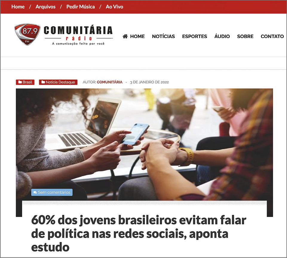 Fotografia. Reprodução de página de internet. Na parte superior o título do site: '87.9 COMUNITÁRIA'. Na parte inferior, fotografia, destacando dois jovens; uma moça segurando um celular ao lado de uma pessoa com as mãos juntas e um dos braços apoiado sobre uma perna. Abaixo, a manchete: '60% dos jovens brasileiros evitam falar de política nas redes sociais, aponta estudo'.