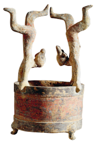 Imagem: Fotografia. Um vaso que apresenta a figura esculpida de duas mulheres de ponta cabeça, apoiados com as mãos na borda e as pernas para o alto.  Fim da imagem.