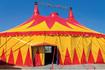 Imagem: Fotografia. Destaque de uma grande tenda de circo vermelha e amarela. Fim da imagem.