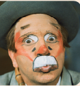 Imagem: Fotografia. Retrato de um homem com rosto pintado, que faz careta usa chapéu. Fim da imagem.