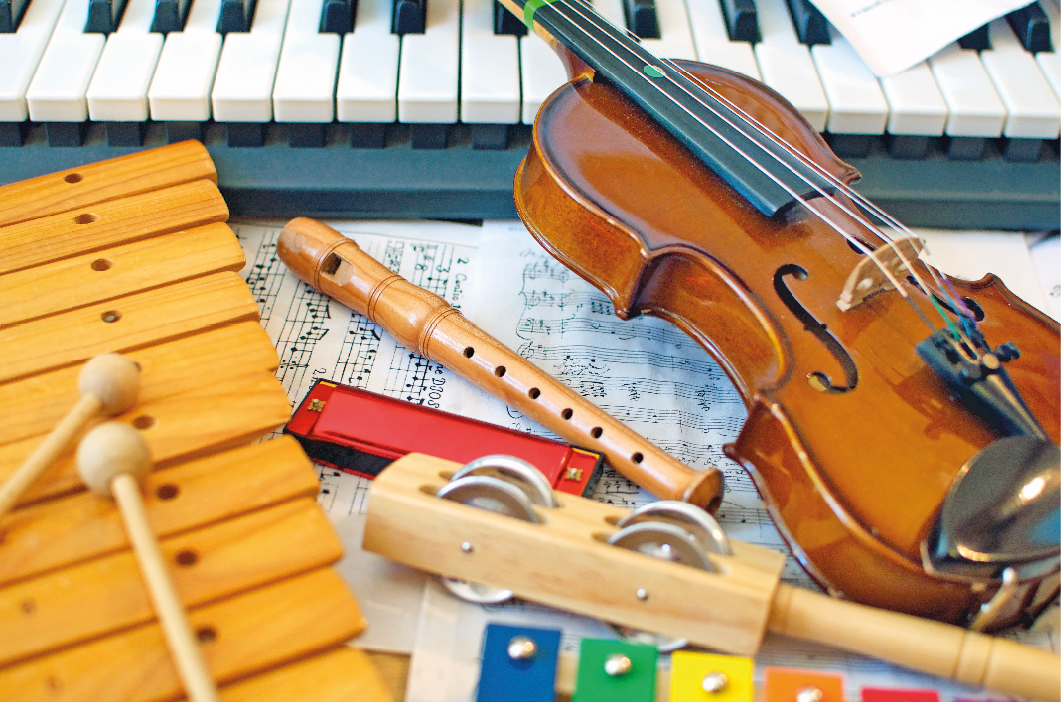 Imagem: Fotografia. Uma composição com partitura, gaita, flauta, teclado, chocalho, xilofone e um violino.  Fim da imagem.