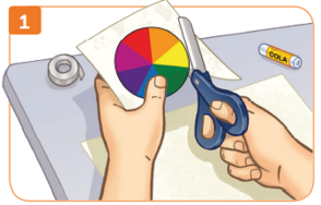 Imagem: Ilustração 1. Destaque das mãos de uma pessoa que recorta o disco colorido com uma tesoura. Na mesa, há cola, papel e fita adesiva. Fim da imagem.