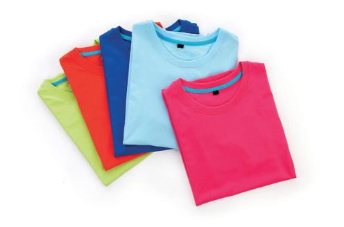 Imagem: Fotografia. Cinco camisetas dobradas uma sobre a outra de cor vermelha, azul-claro, azul-escuro, laranja e cinza-claro.  Fim da imagem.