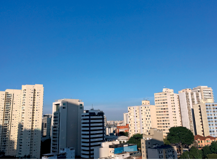 Imagem: Fotografia. A mesma cidade descrita anteriormente. O céu está de cor azul, sem nuvens.  Fim da imagem.
