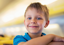 Imagem: Fotografia. Um menino loiro de olhos azuis, com camiseta de gola em azul-claro, visto dos braços para cima, cruzados. Fim da imagem.