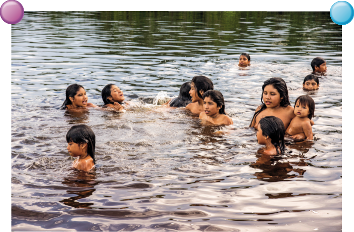 Imagem: Fotografia. Dentro de um rio de cor escura com dezenas de crianças nadando e brincando, meninos e meninas de pele morena e cabelos pretos.  Fim da imagem.