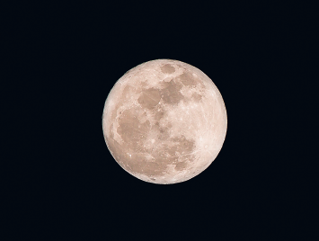 Imagem: Fotografia 2. Fundo em preto com lua redonda de cor bege-claro com partes em bege-escuro na esquerda e centro.  Fim da imagem.