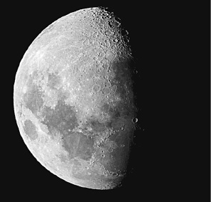 Imagem: Fotografia. Lua redonda com grande parte à esquerda de cor cinza-claro, com partes com manchas em cinza-escuro. Na parte direita, sombra de cor preta.  Fim da imagem.