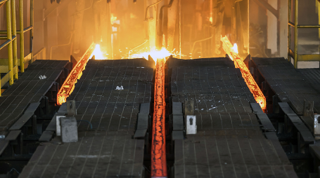 Imagem: Fotografia. Estrutura na horizontal de cor preta, com três fendas na vertical com chama de cor laranja. Ao fundo, fogo com chamas incandescentes em amarelo. Fim da imagem.