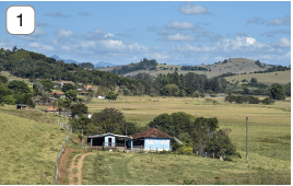 Imagem: Fotografia 1. Vista geral de local com grama de cor verde, uma casa de paredes brancas, com telhado de cor marrom, com árvores de folhas em verde-escuro ao redor. Mais ao fundo, árvores e morros com vegetação. No alto, céu azul-claro com nuvens brancas. Fim da imagem.