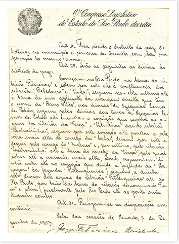 Imagem: Fotografia em preto e branco. Uma folha branca com texto grande escrito e letra cursiva, de cor preta em português antigo. No alto, título: O congresso legislativo do Estado do São Paulo decreta. Primeiro parágrafo: Art 1° Fica creado o districto de paz de bolliva no município e comarca de Barretos, com sede na povoação do mesmo nome.  Art.2° serão as seguintes as divisas do districto de paz. [...]  Fim da imagem.