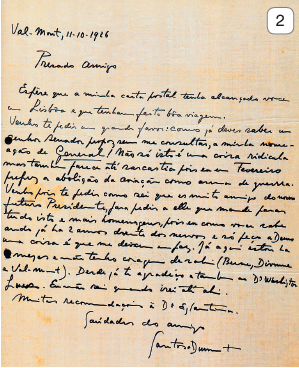 Imagem: Fotografia 2. Um papel de cor bege, com texto manuscrito de cor preta, em letras cursivas. A letra é ilegível.  Fim da imagem.