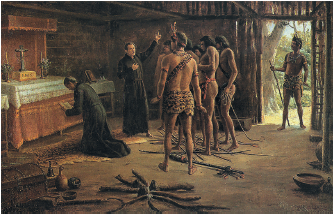 Imagem: Pintura. Dentro de uma toca, moradia de paredes de madeiras com palhas e solo em terra.  Na parte interna da toca, dois homens com vestes de religiosos de cor preta à esquerda. Um deles está agachado de joelhos e segurando nas mãos uma bíblia, de frente para um púlpito de lenço branco e parte vermelha, com uma cruz. À direita, religioso em pé de pele clara, cabelos escuros, com vestes longas em preto, com o braço direito para o alto e braço esquerdo sobre o peito. De frente para eles, dezenas de indígenas em pé. Eles têm pele morena, com coroa de plumas e saiote na cintura. Ao fundo, à direita, porta e um indígena em pé, segurando uma vara na mão esquerda de madeira. Em terceiro plano, árvores com folhas verdes.  Fim da imagem.