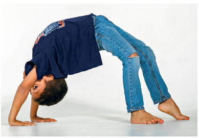 Imagem: Fotografia. Um menino usando camiseta e calça jeans. Ele está com as mãos e pés no chão e o tronco fazendo um arco com a barriga para cima. Fim da imagem.