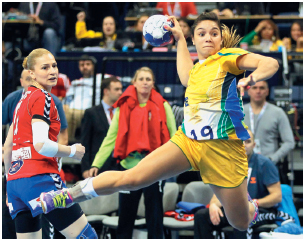 Imagem: Fotografia. À esquerda, uma mulher com uniforme vermelho e azul. Ele está de perfil, olhando para uma mulher, que está usando uniforme amarelo, segurando a bola com a mão esquerda e saltando com o braço estendido para trás. Fim da imagem.